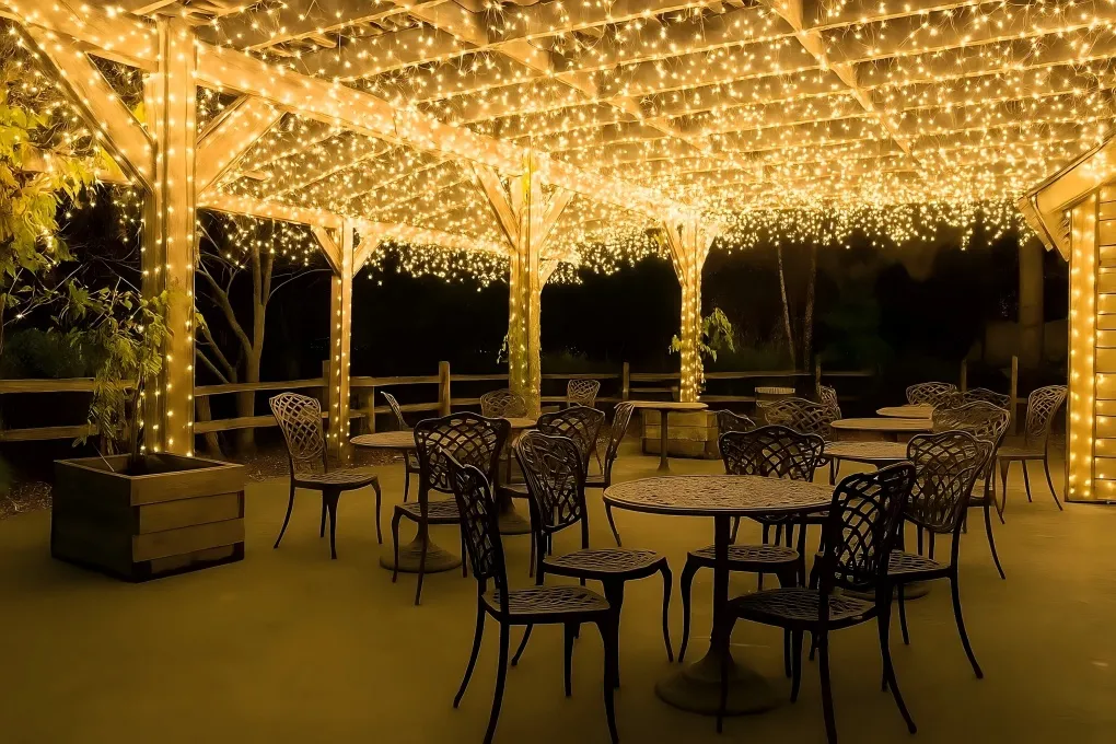 Pergola adorned with delicate fairy lights wrapped around plants and placed in glass jars, creating a whimsical and enchanted outdoor ambiance.
